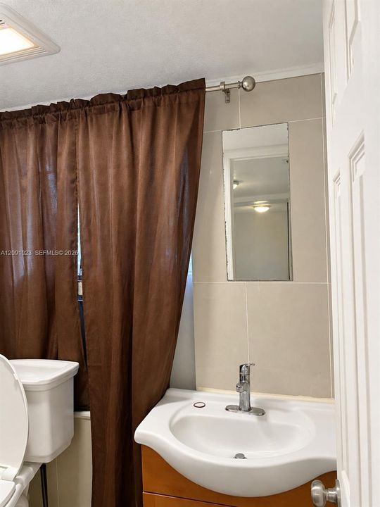 Wall-mounted rectangular mirror, ceramic sink basin with a single-handle chrome faucet, wood-finish cabinetry, and neutral-toned wall tiling