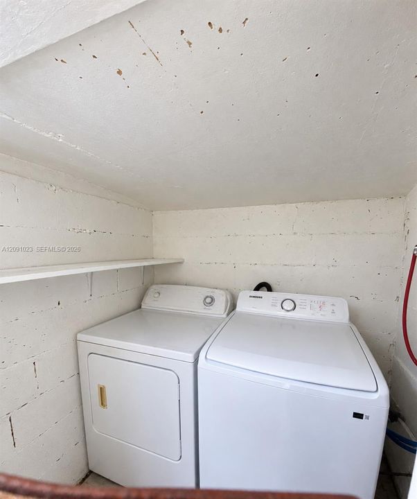 Laundry area featuring white top-load appliances and an integrated wall-mounted shelf against a painted masonry finish