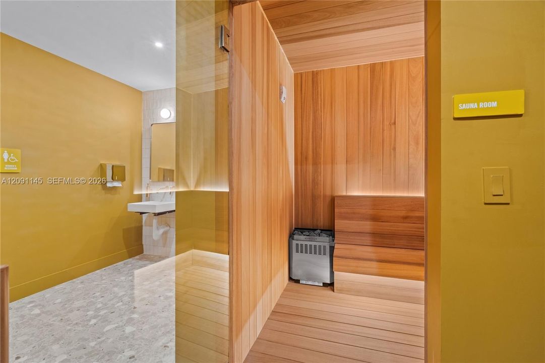 Sauna room featuring wood-paneled walls and bench, with a stone-fill electric heater