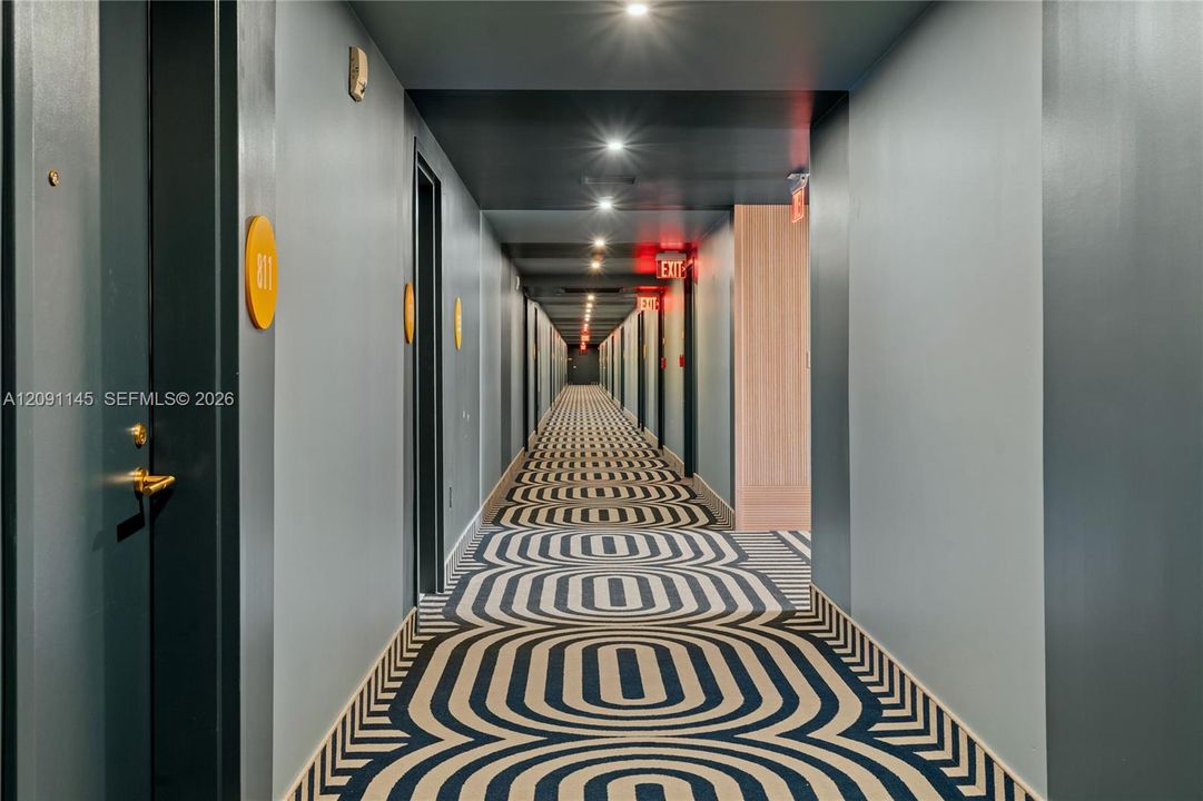 Hallway with patterned carpet, recessed lighting, and wall-mounted room indicators