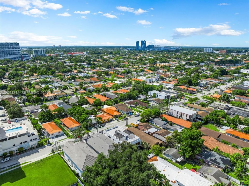 Aerial perspective featuring an established urban residential grid, mature canopy trees, and high-rise metropolitan skyline in the distance