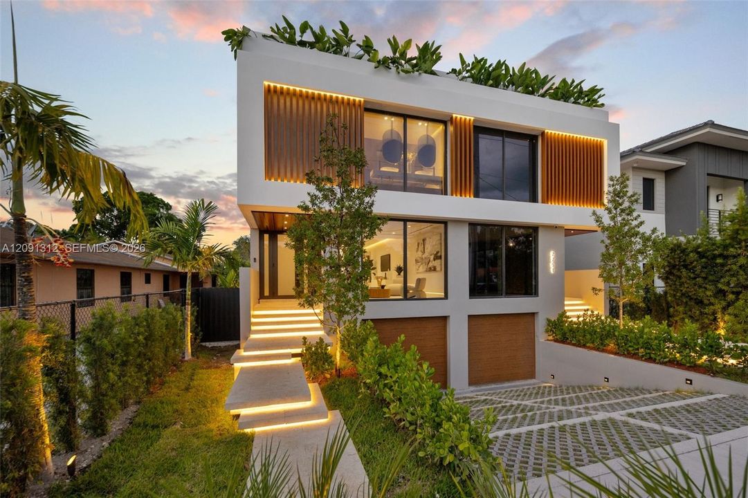 Modern two-story architectural exterior featuring smooth white stucco finish, vertical wood-slat accents, integrated LED stair and facade lighting, large-format glass sliders, and a permeable paver driveway