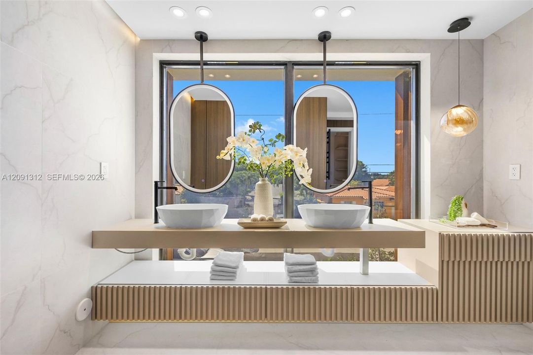 Floating vanity featuring dual vessel sinks, matte black wall-mounted faucets, oval-shaped hanging mirrors, and fluted wood-finish cabinetry with built-in storage