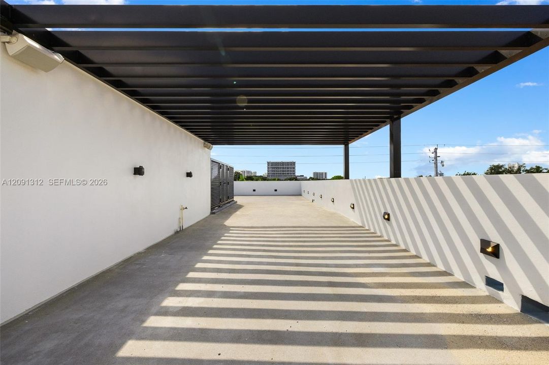 Rooftop terrace featuring a black metal pergola, concrete flooring, exterior wall-mounted lighting, and solid perimeter walls