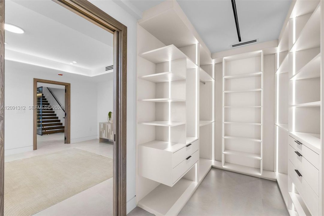 Custom walk-in closet featuring floor-to-ceiling built-in shelving, integrated vertical LED lighting, and drawer storage with matte black hardware