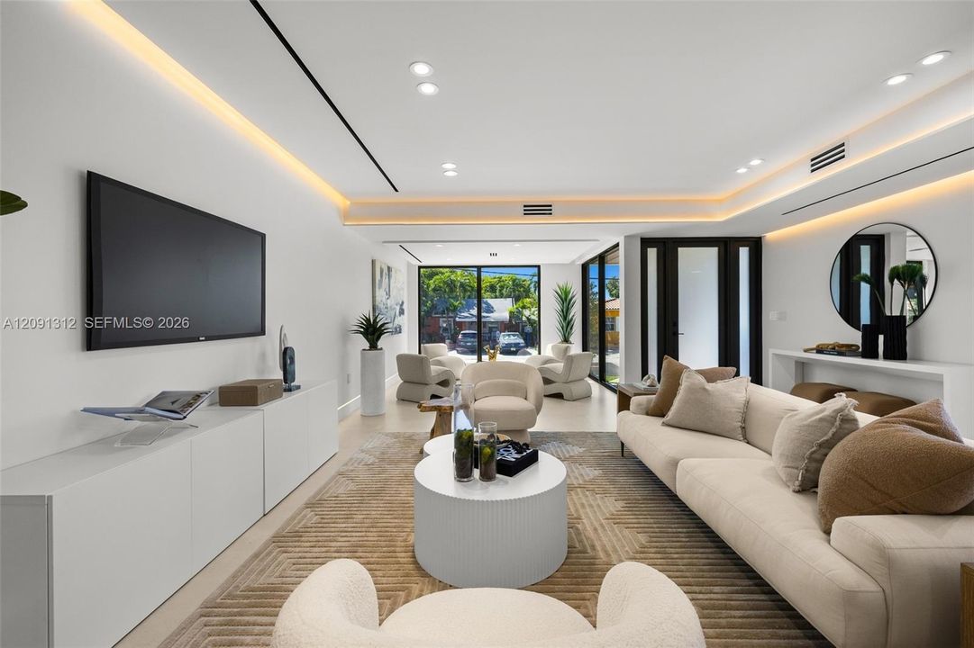 Living area featuring recessed LED cove lighting, recessed ceiling lighting, large-format tile flooring, and floor-to-ceiling glass panel doors