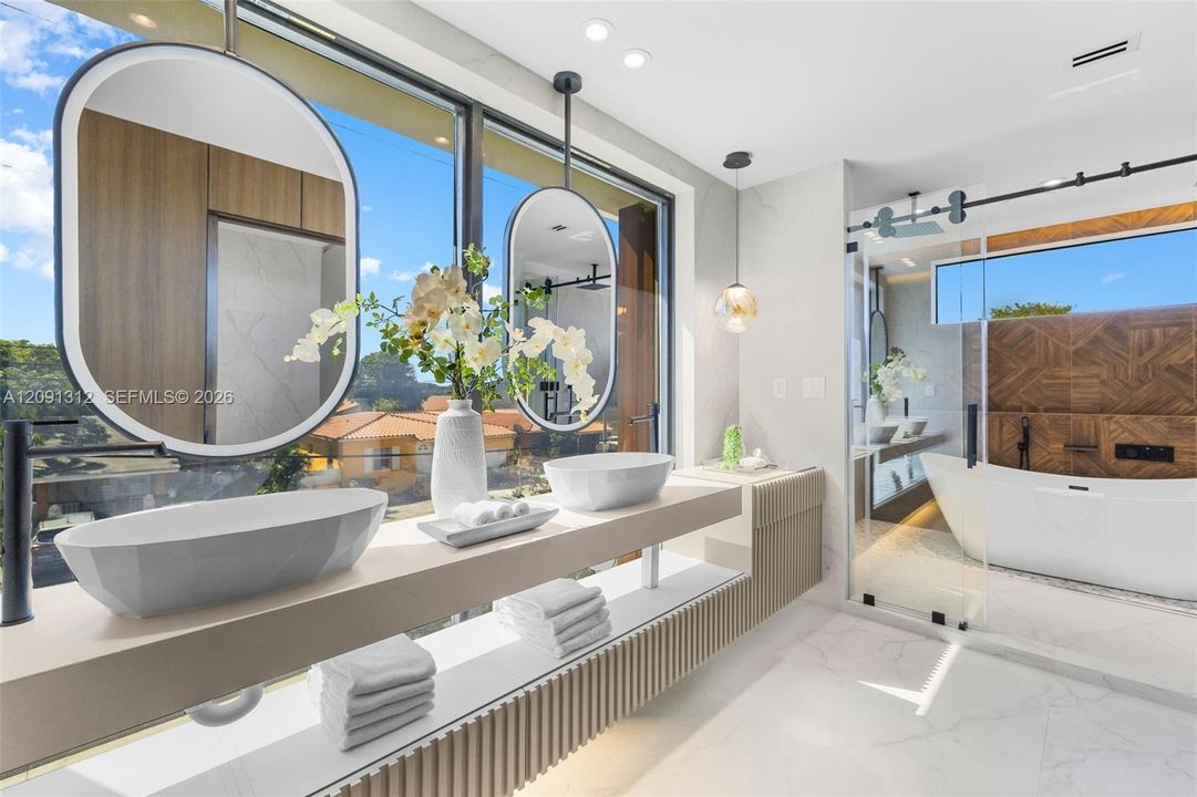 Floating dual-vanity featuring rectangular vessel sinks and pendant-style mirrors, paired with a glass-enclosed soaking tub and stone-tile flooring