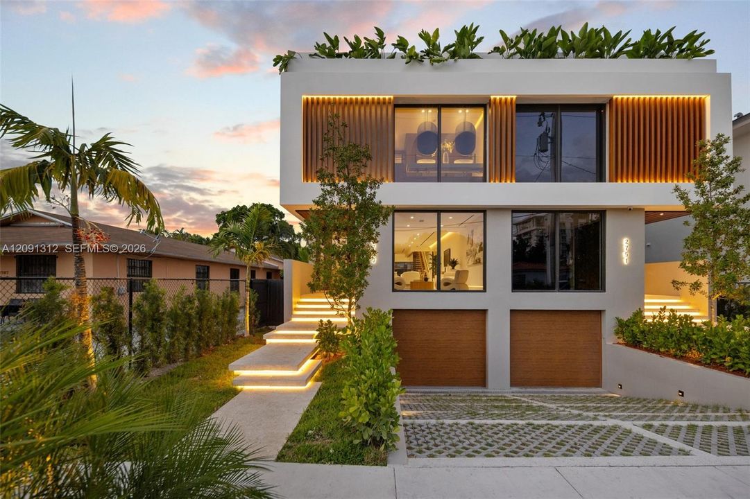 Modern multi-level exterior featuring clean-lined smooth stucco, vertical slat accents, dual garage doors with wood-finish surfacing, tiered concrete steps with integrated lighting, and a flat roofline with built-in perimeter planter boxes