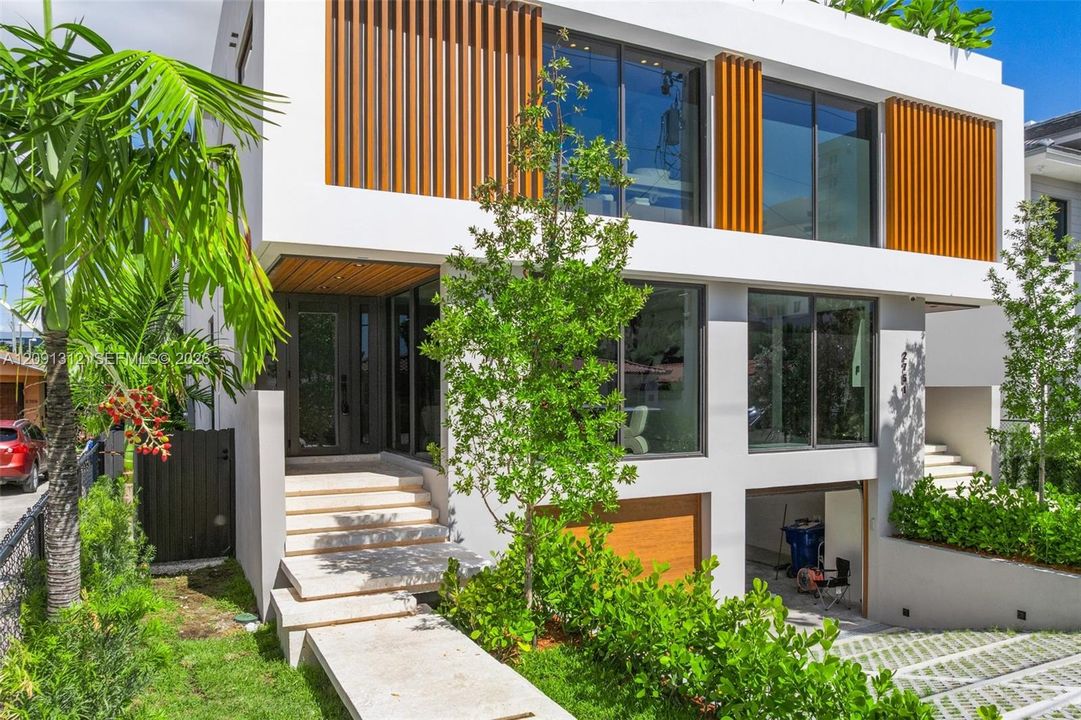 Contemporary exterior featuring clean-lined white stucco, vertical wood-finish louvers, expansive floor-to-ceiling windows, a stone-paved entry staircase, and a tiered driveway with permeable pavers