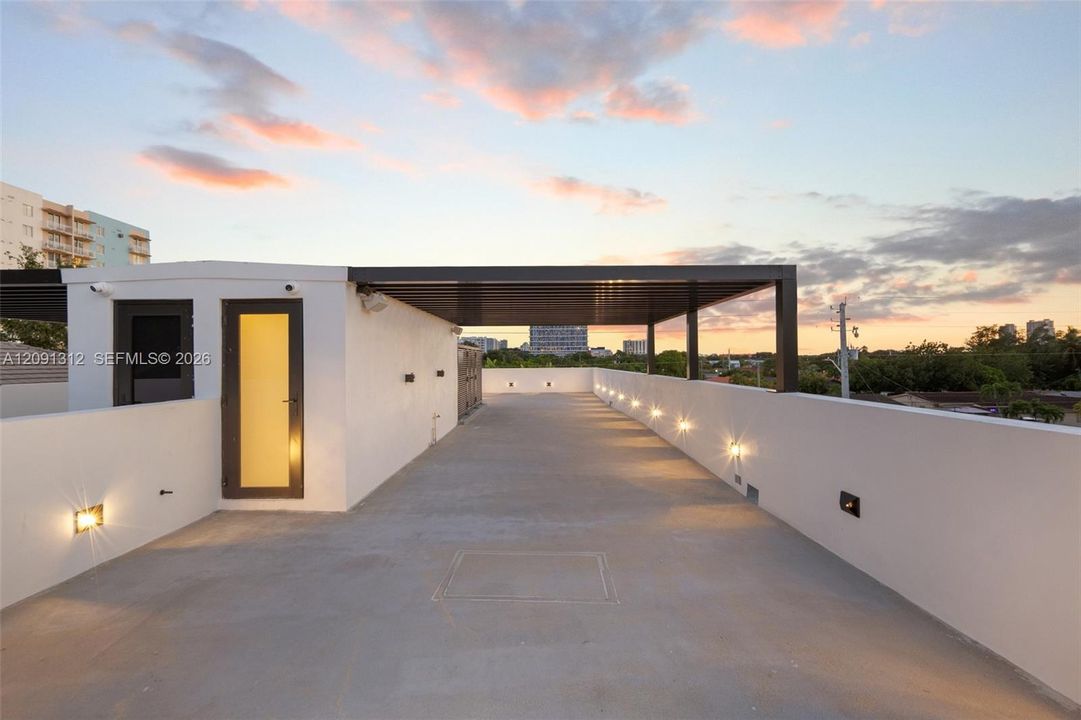 Rooftop terrace featuring smooth concrete flooring, solid perimeter walls, built-in wall-mounted lighting, and a metal-framed covered area