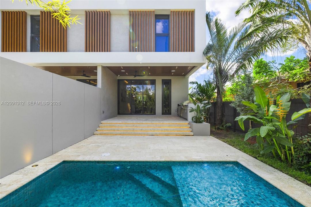 Modern exterior featuring vertical wood-slat privacy screens, stone patio with tiered steps, built-in outdoor kitchen, and a tiled swimming pool