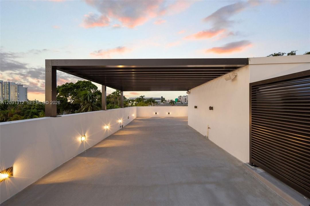 Rooftop terrace featuring a covered pergola, concrete flooring, smooth stucco parapet walls, and integrated wall-mounted lighting