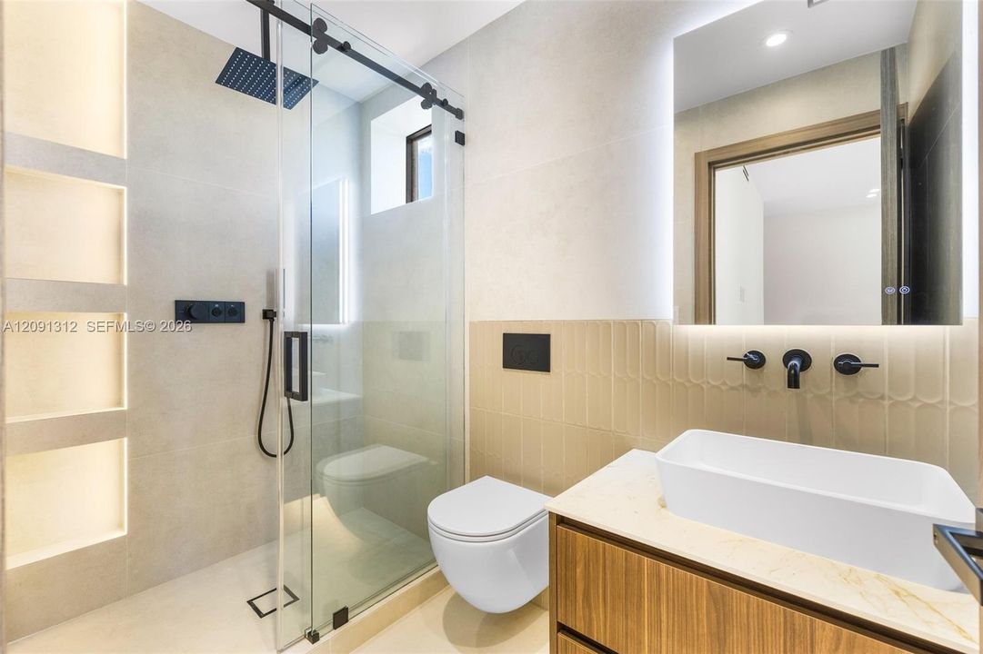 Modern bathroom featuring a wood-finish floating vanity, vessel sink with matte black wall-mounted faucet, wall-mounted toilet, and glass-enclosed shower with integrated recessed shelving