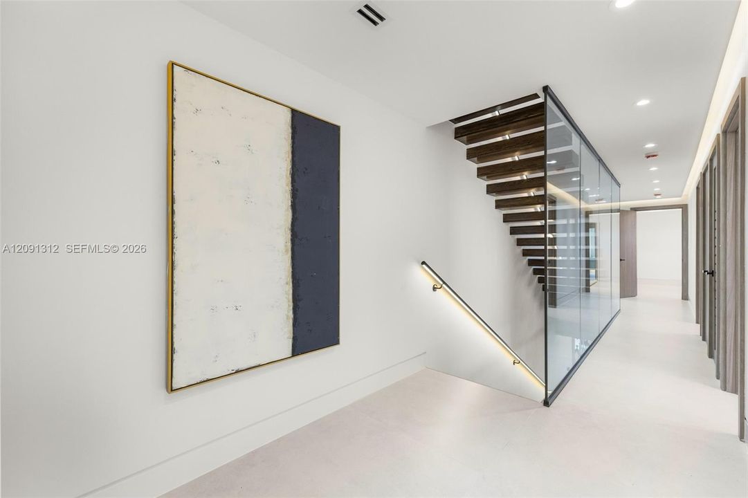 Staircase featuring open-riser wood treads, a full-height glass panel partition, a sleek wall-mounted handrail with integrated LED lighting, and large-format tile flooring