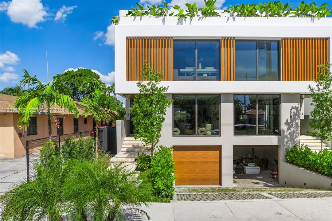 Contemporary two-story exterior featuring a rooftop terrace, wood-slat screening, expansive floor-to-ceiling windows, and a built-in garage with a matching wood-finish door