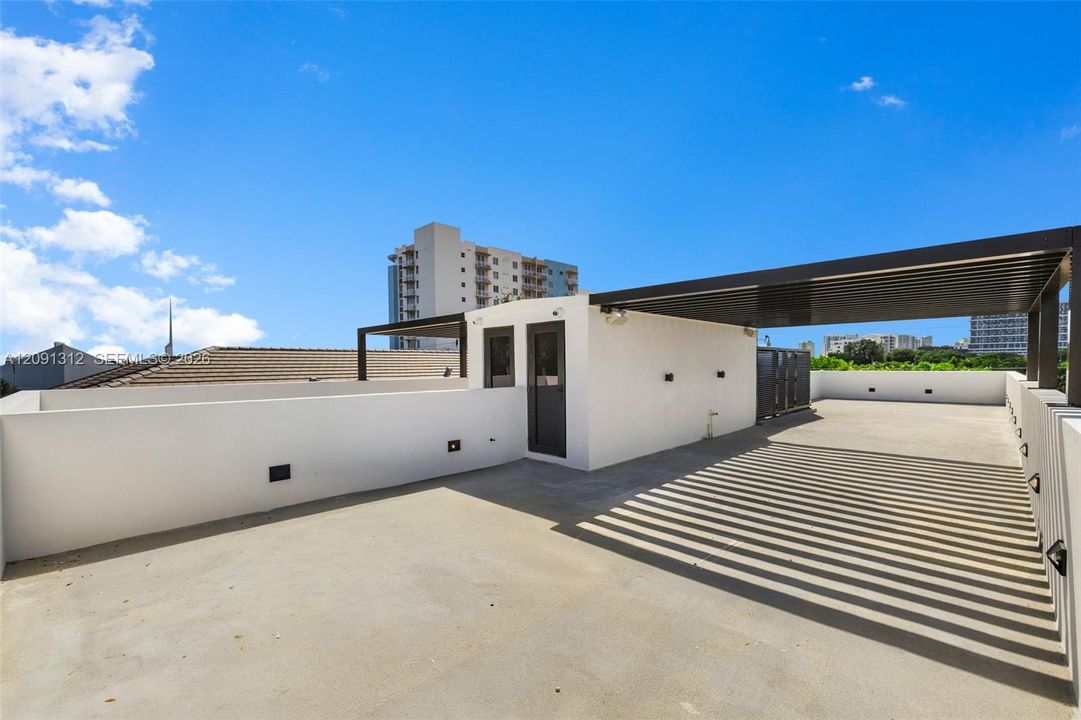 Rooftop terrace featuring concrete flooring, a partial louvered metal pergola, solid perimeter walls, and exterior wall-mounted lighting