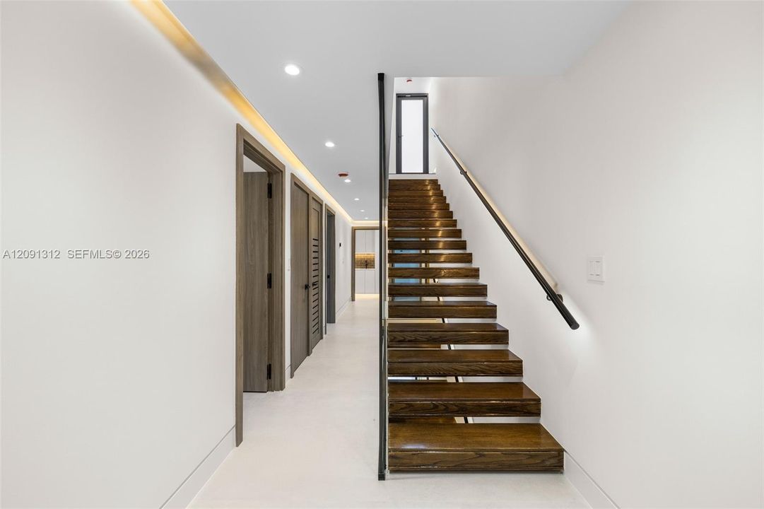 Open-tread staircase featuring wood-finish steps, a minimalist black metal handrail, recessed ceiling lighting, and smooth-finish flooring