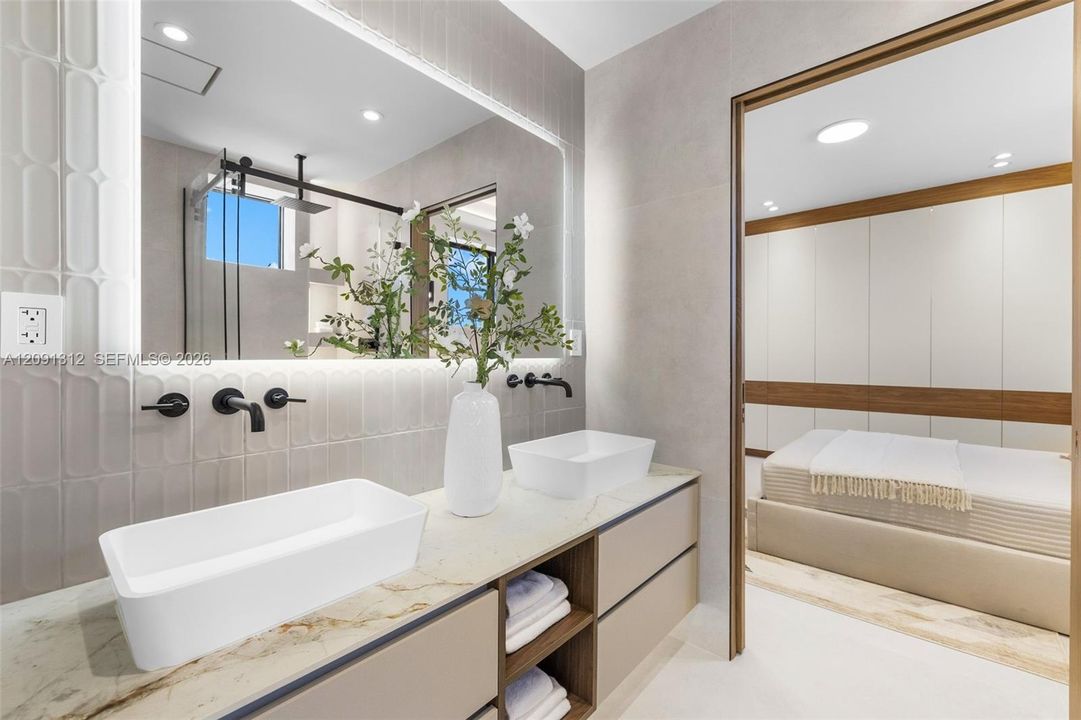 Double vanity featuring stone countertops, rectangular vessel sinks, matte black wall-mounted faucets, integrated under-cabinet lighting, and textured wall tile