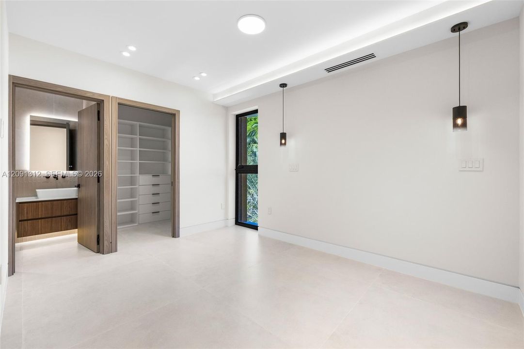 Interior space featuring large-format tile flooring, recessed ceiling lighting, dual pendant fixtures, and a walk-in closet with custom built-in shelving