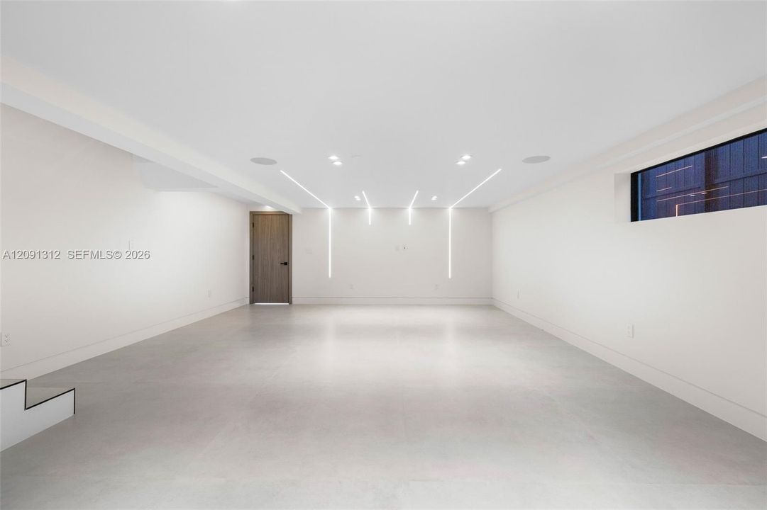 Open interior featuring expansive smooth-surface flooring, integrated recessed linear LED accent lighting, minimalist high-ceiling design, and a solid-core wood-finish door with matte black hardware