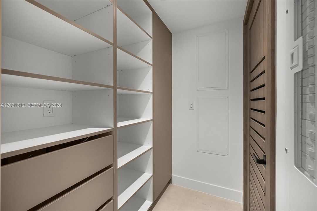 Custom built-in storage unit featuring adjustable shelving, integrated soft-close drawers, and a neutral wood-finish frame, complemented by a louvered-style door