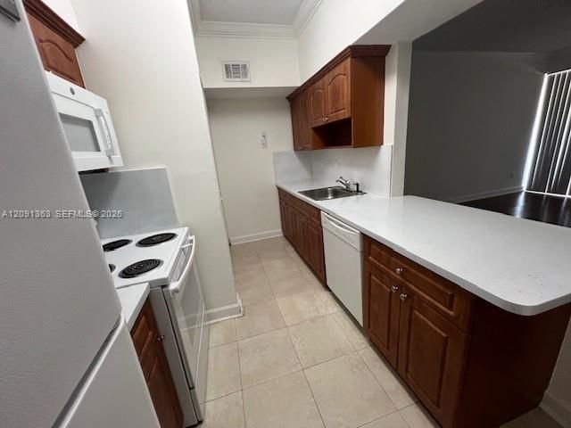 Kitchen featuring wood cabinetry, white solid-surface countertops, tile flooring, and integrated white appliances