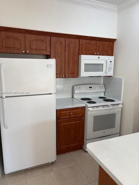 Kitchen featuring wood-finish cabinetry, solid surface countertops, white appliances, and tiled flooring