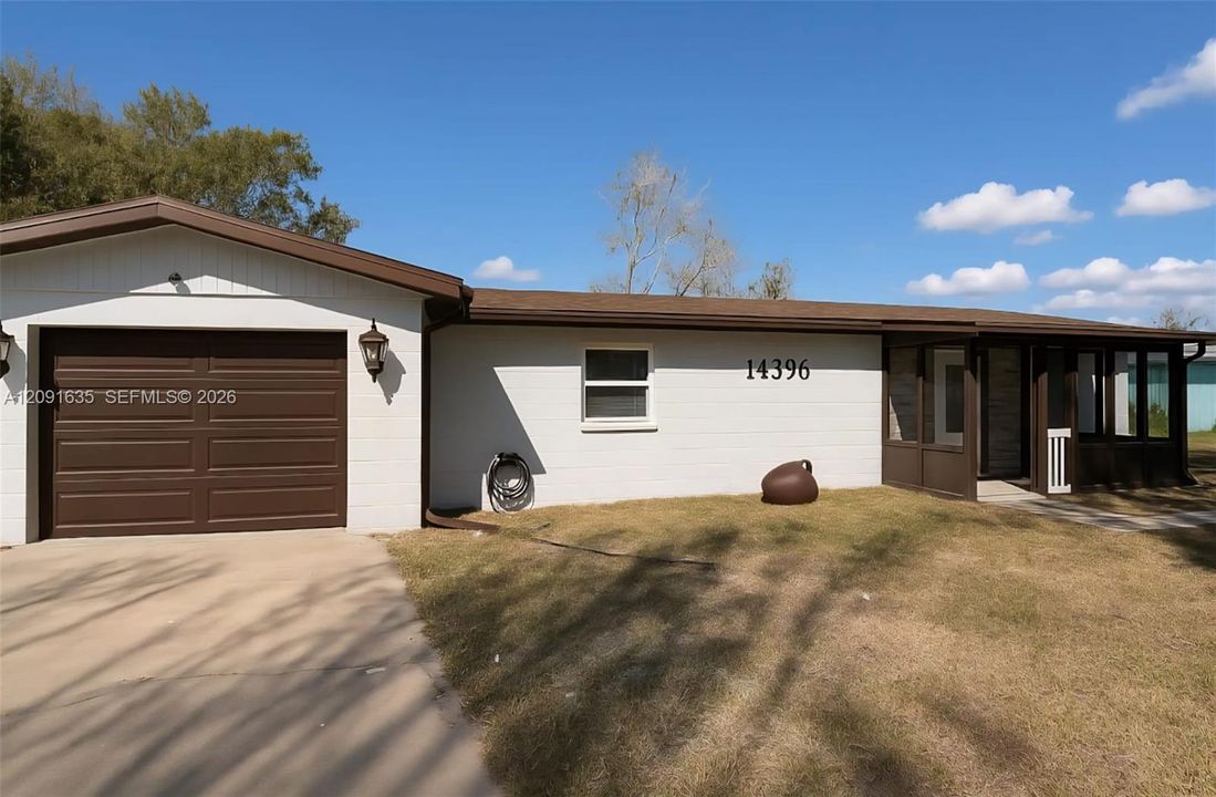 Beautiful front exterior showcasing the clean landscaping, attached garage, and welcoming screened front porch under the Florida sun