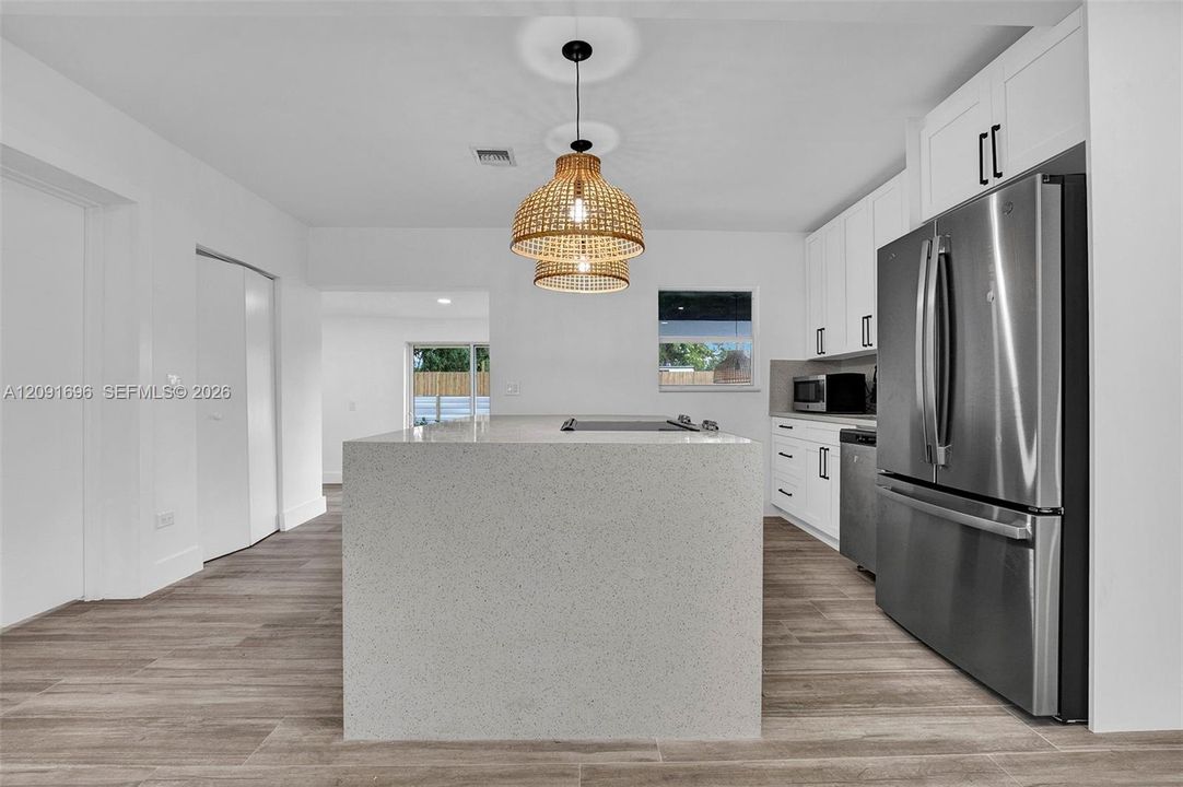 Kitchen featuring an expansive center island with a stone-finish countertop, stainless steel appliances, white cabinetry with matte black hardware, and wood-finish flooring