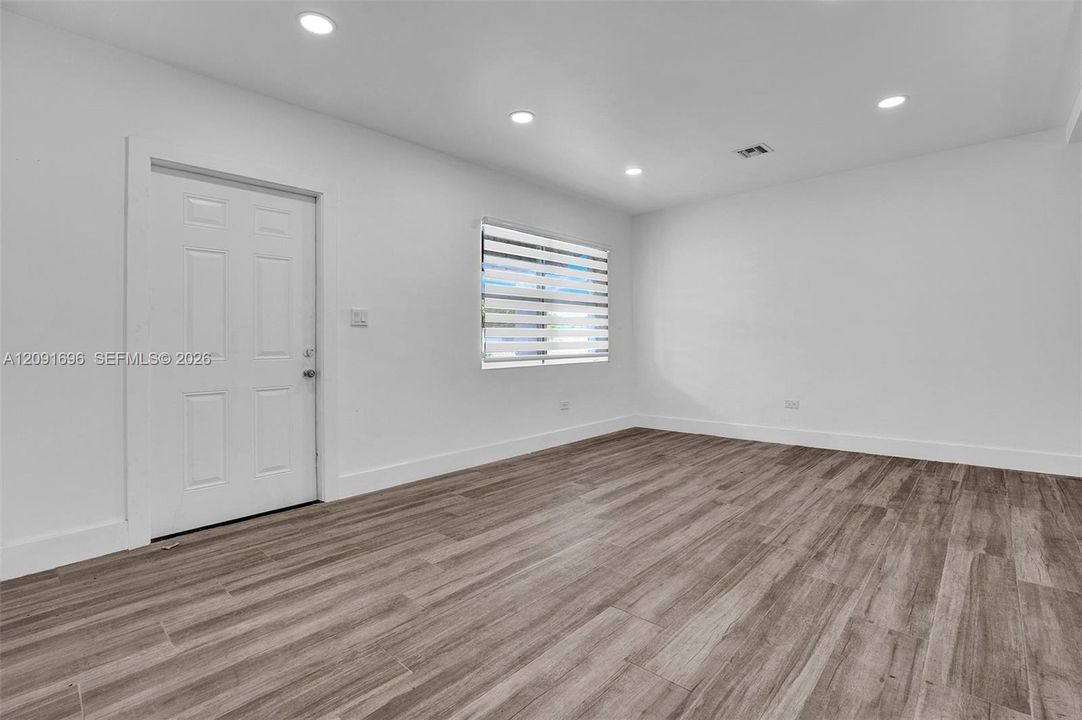 Neutral-toned interior space featuring wood-finish flooring, recessed lighting, and a solid-panel door