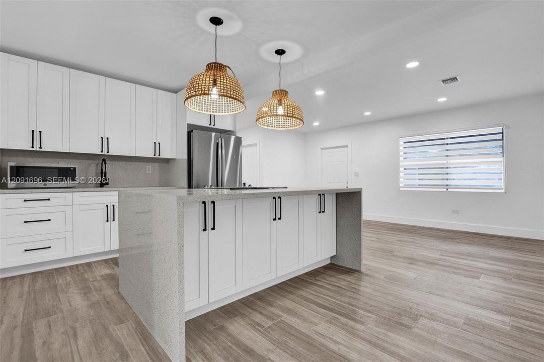 Kitchen featuring white Shaker-style cabinetry, a quartz-surfaced waterfall island, wood-finish flooring, recessed lighting, and woven pendant fixtures