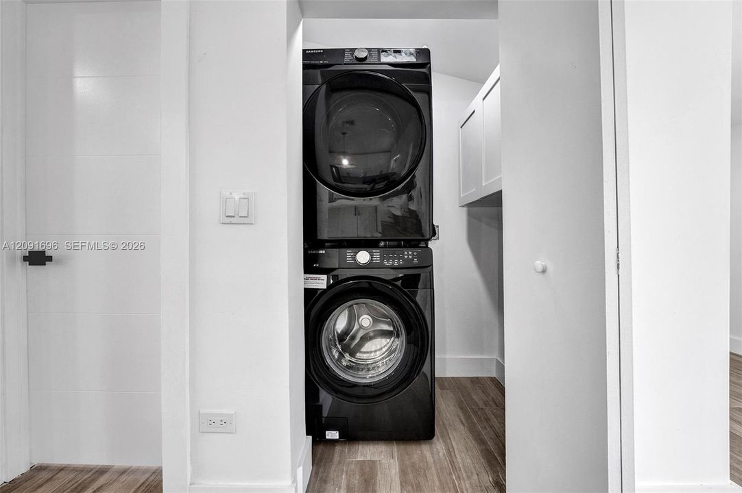 Laundry nook featuring a stacked washer and dryer unit, wood-finish flooring, and white wall-mounted cabinetry