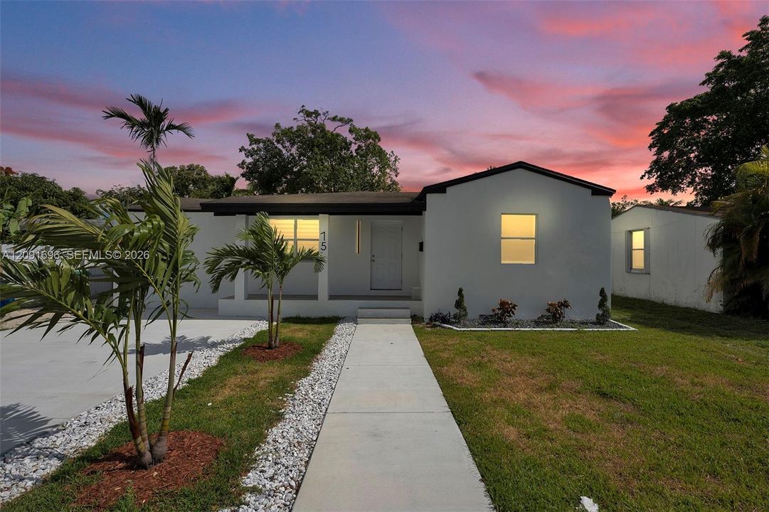 Single-story residence featuring a smooth stucco exterior, a covered front entryway, a concrete walkway, and decorative stone landscaping accents