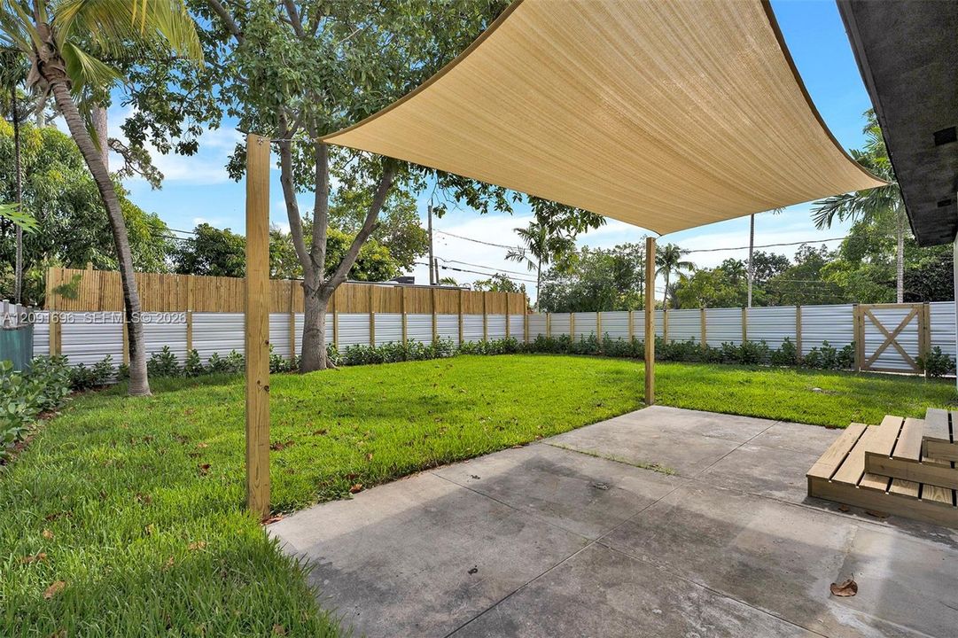 Backyard featuring a concrete patio, wood-framed shade sail, wood-step entry, and white corrugated metal fencing
