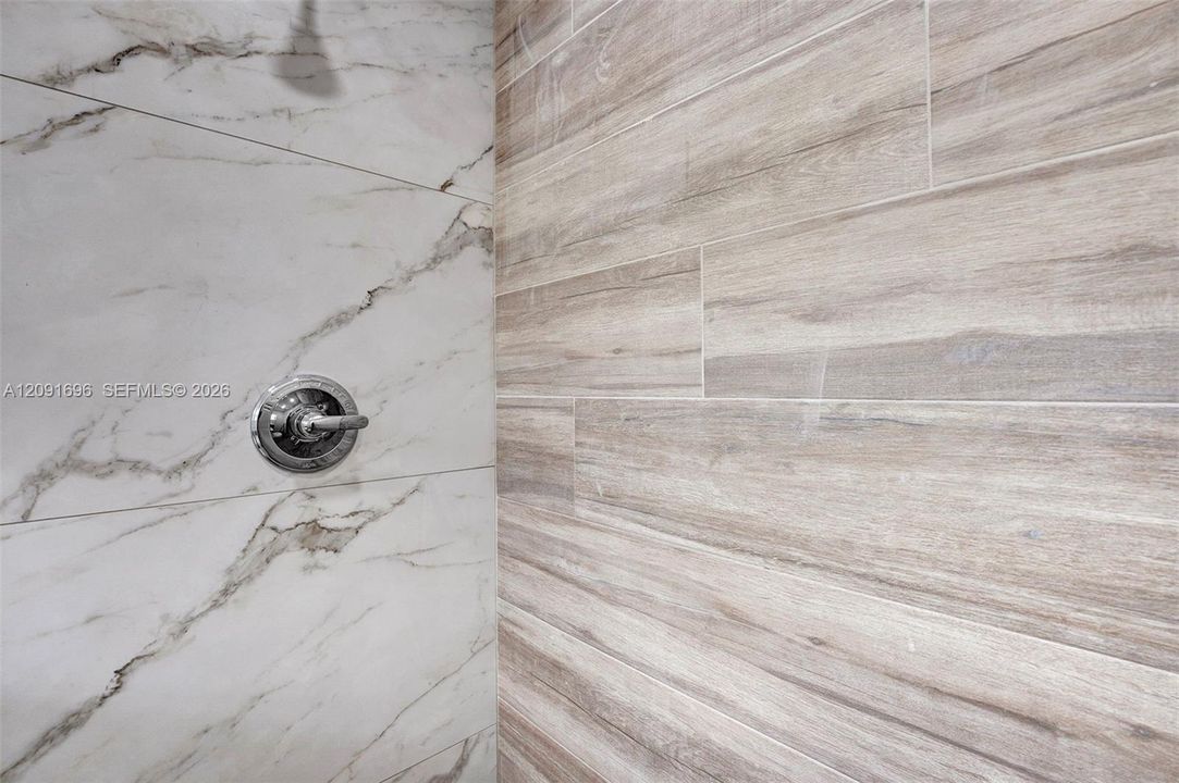 Shower enclosure featuring large-format stone-patterned wall tile, wood-finish wall tile, and a circular chrome shower control valve