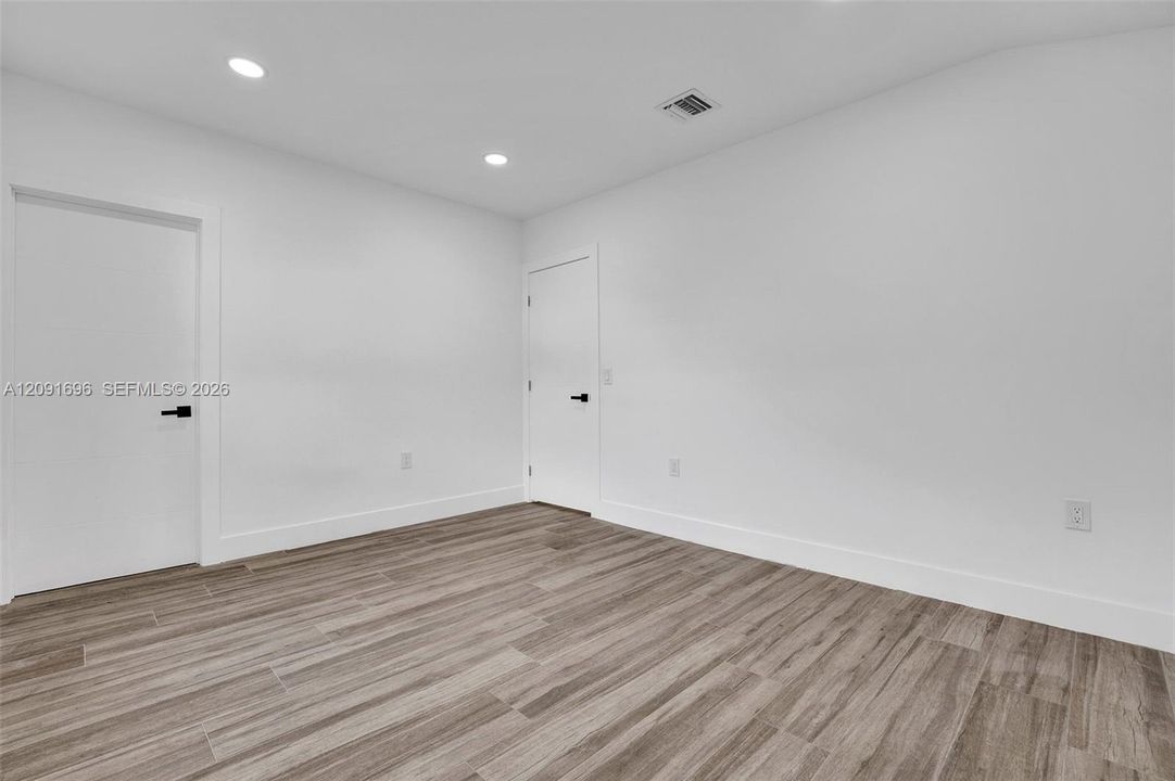 Interior space featuring wood-finish flooring, neutral white walls, recessed ceiling lighting, and solid-core doors with matte black hardware