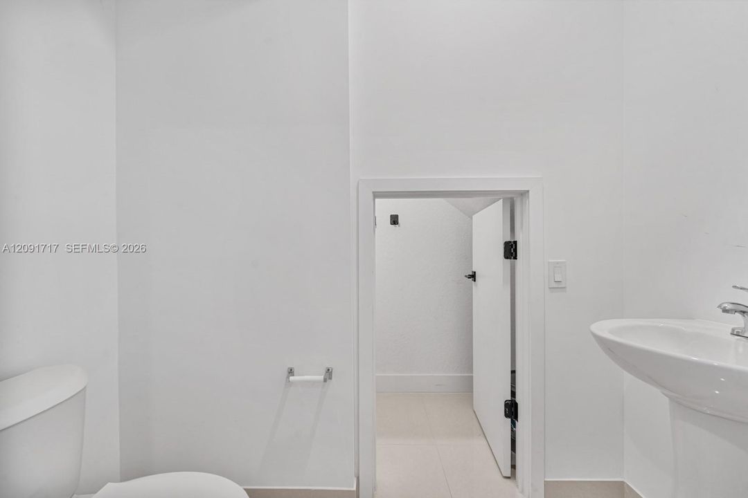 Pedestal sink with chrome faucet, porcelain toilet, and interior access door with matte black hardware