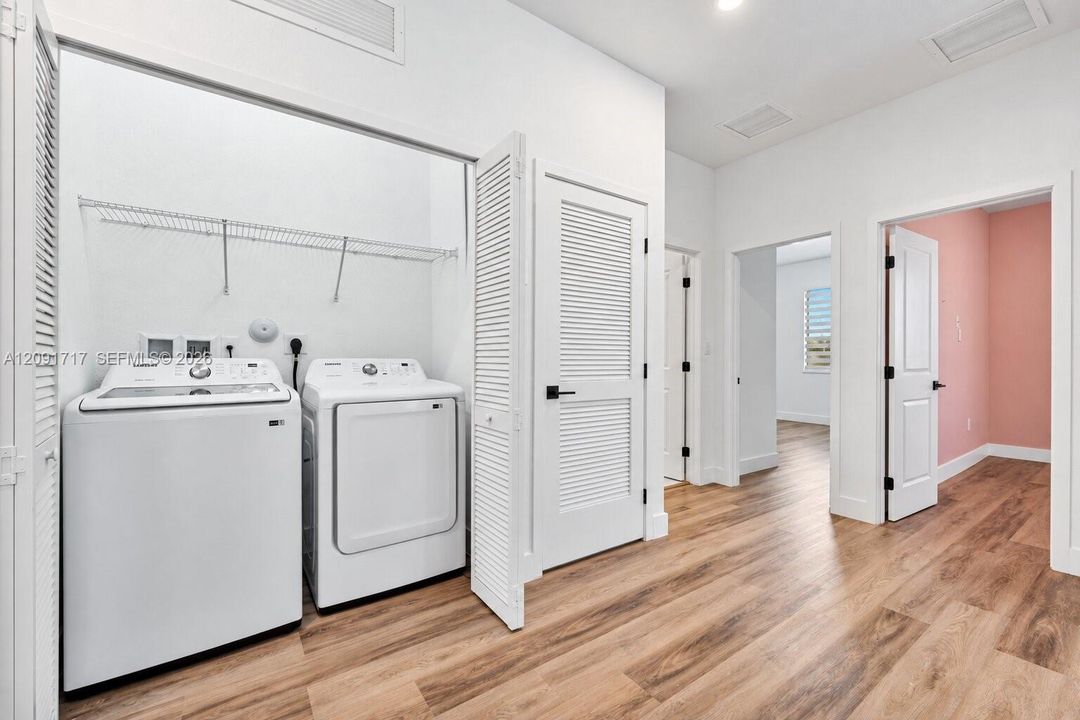 Laundry area featuring wood-finish flooring, white louvered closet doors, and overhead wire shelving