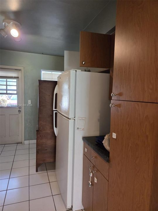 Wood-finish cabinetry, floor-to-ceiling pantry storage, ceramic tile flooring, and multi-light ceiling fixture
