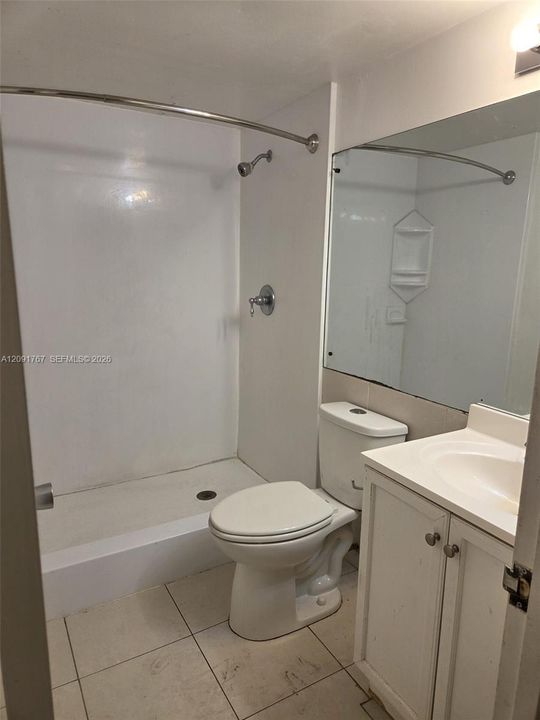 Bathroom featuring a walk-in shower with integrated shelving, white cabinetry, a single-basin vanity, and large-format tile flooring