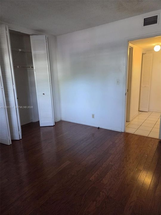 Room featuring dark wood-finish flooring, a built-in closet with louvered bifold doors, and a doorway opening to a tiled area