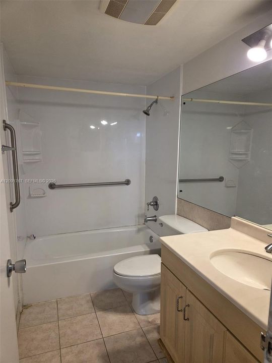Full-width vanity with integrated countertop and sink, large wall-mounted mirror, tub-shower combination with surround, and ceramic tile flooring