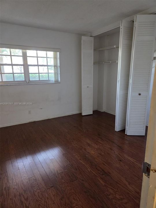 Wood-finish flooring, multi-pane window, and closet featuring white louvered bi-fold doors with built-in wire shelving