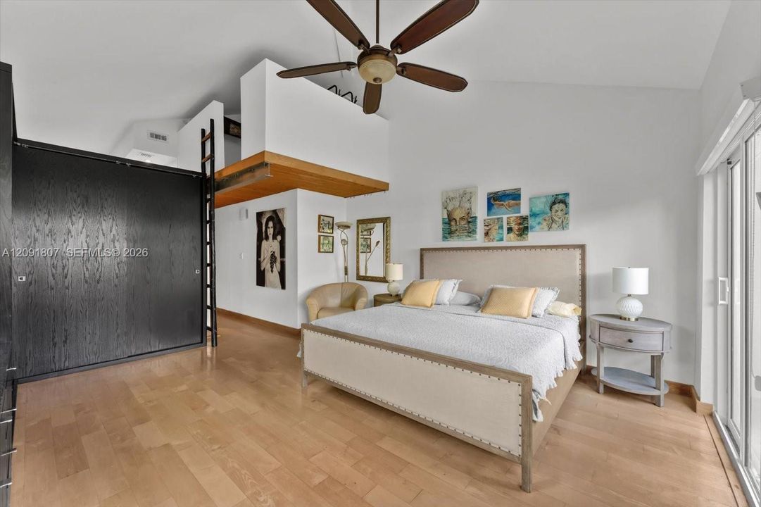 Vaulted ceilings featuring a prominent ceiling fan, wood-finish flooring, floor-to-ceiling dark-finish cabinetry, a built-in ladder, and sliding glass doors
