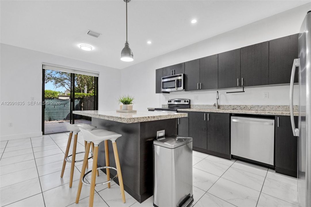 Kitchen featuring dark-toned flat-panel cabinetry, stone countertops, stainless steel appliances, a center island, and large-format tile flooring