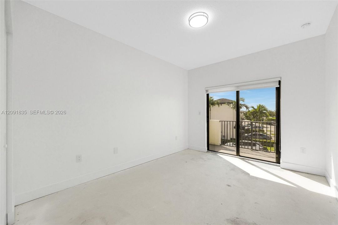 Interior space featuring neutral wall paint, flush-mount ceiling lighting, and sliding glass doors opening to a balcony with metal railings