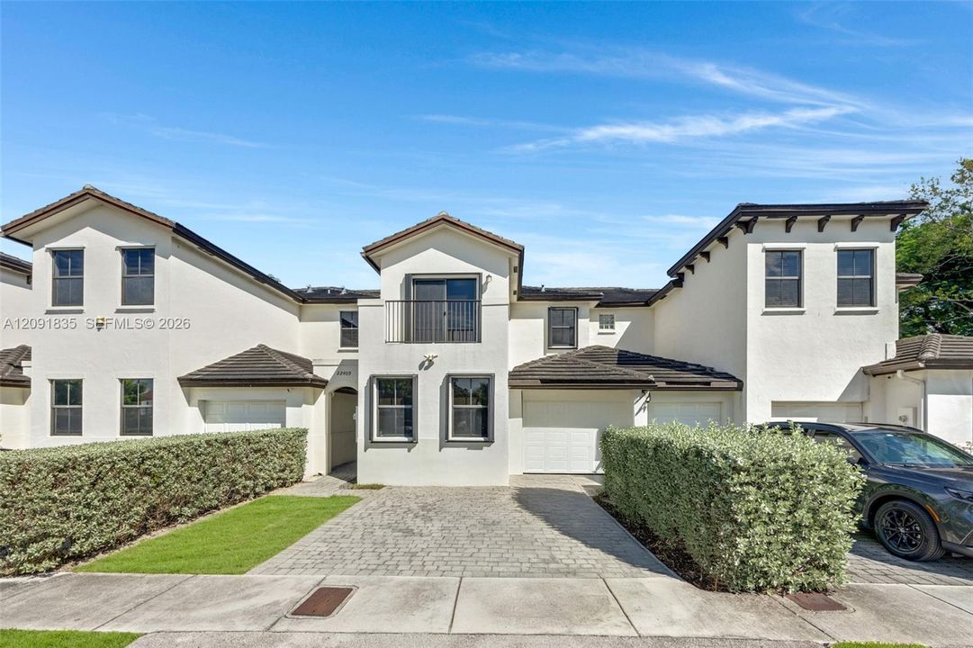 Stucco exterior featuring multiple attached garage bays, a paved driveway, and an upper-level balcony with metal railings