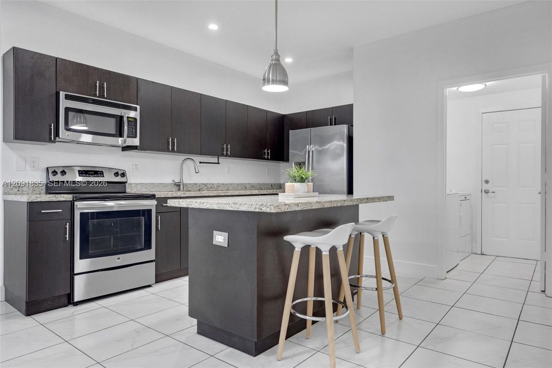 Kitchen featuring dark-finish cabinetry, stone-style countertops, stainless steel appliances, a central island, and ceramic tile flooring