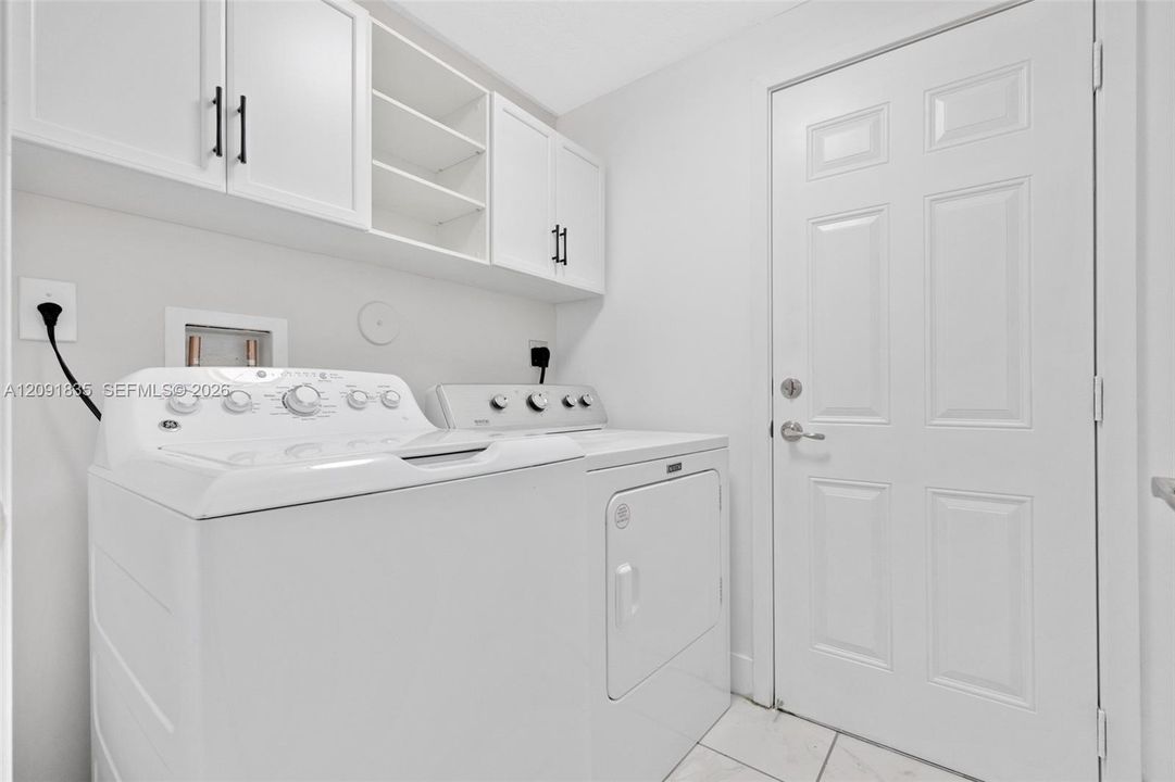 Laundry area featuring white shaker-style wall cabinets with matte black hardware, open shelving, and tile flooring