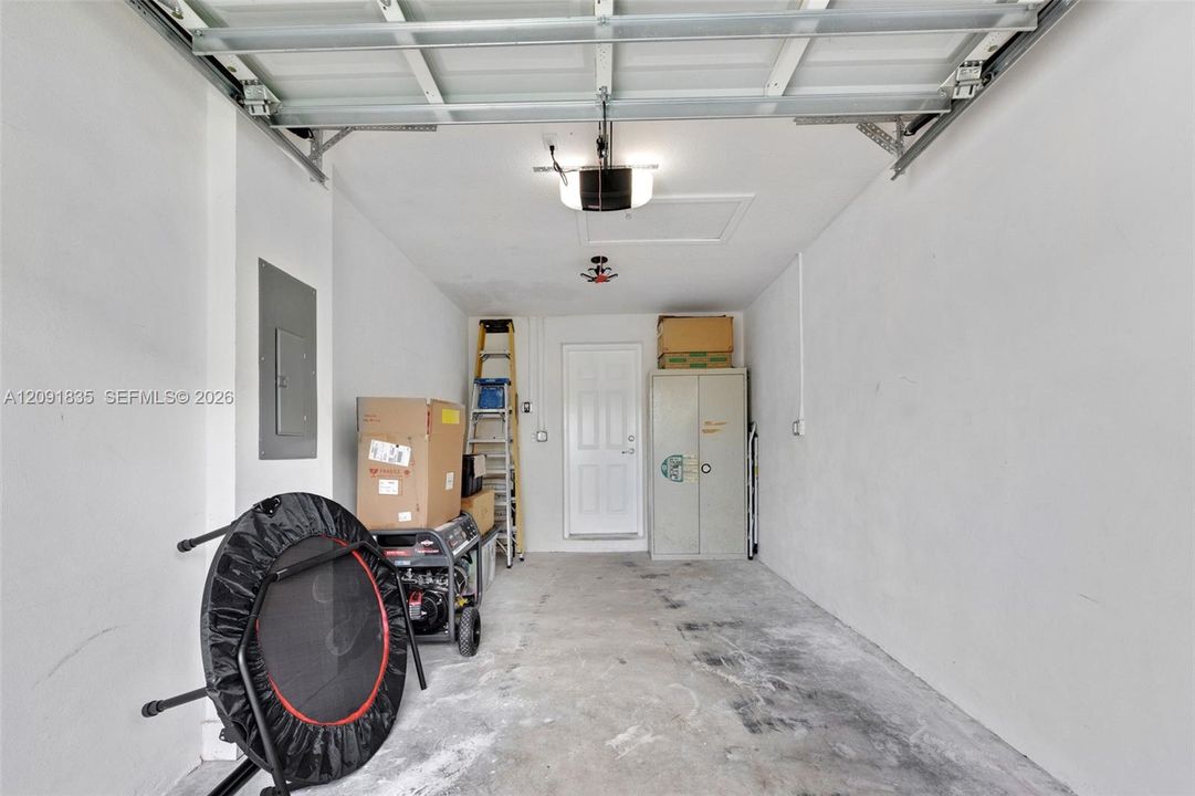 Garage interior featuring a concrete floor, automated overhead door system, ceiling-mounted lighting, integrated electrical panel, and a paneled service door